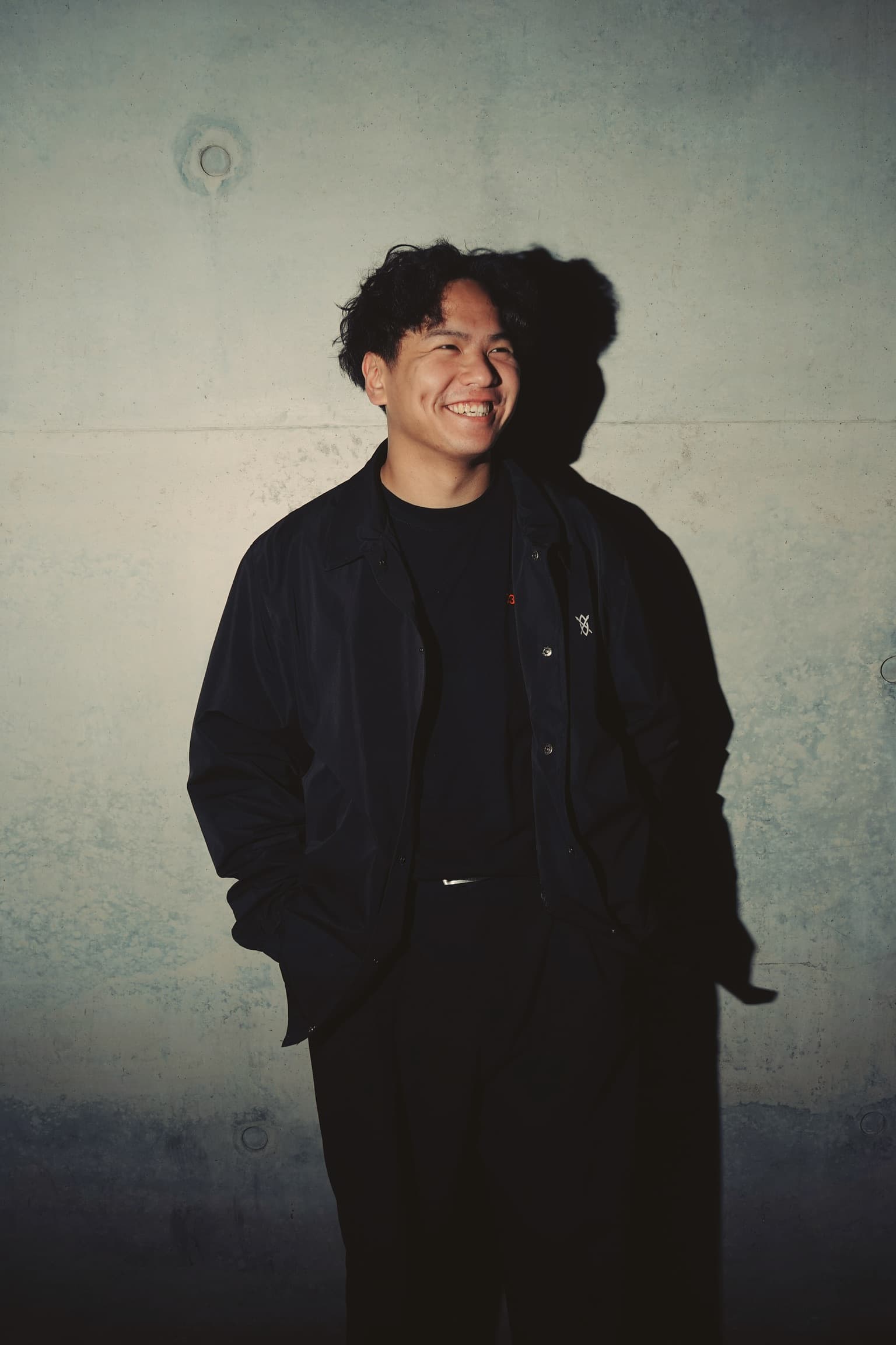 GESHA laughing against a concrete wall